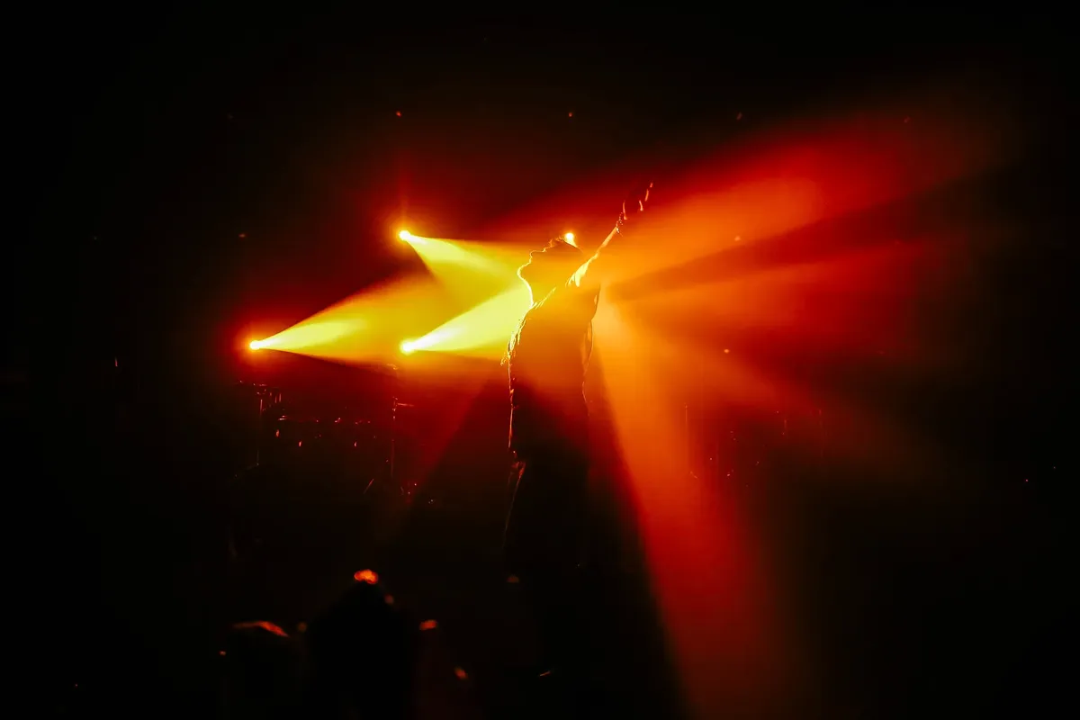 Silhouette of a performer on stage with vibrant spotlight beams creating dramatic concert atmosphere.
