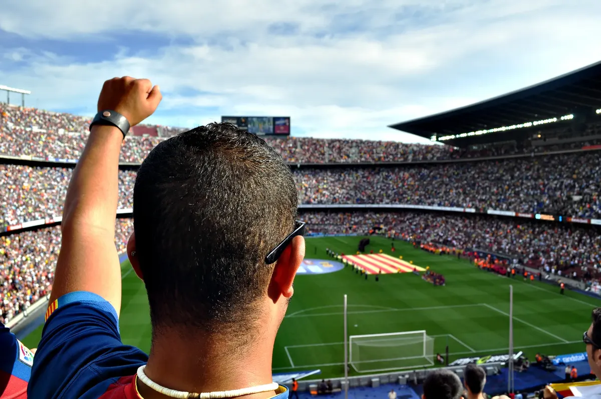 A passionate football fan cheers among a crowd at a bustling stadium, creating an electrifying atmosphere.
