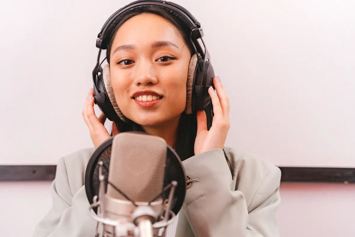 Female artist recording music in studio with condenser microphone and headphones.