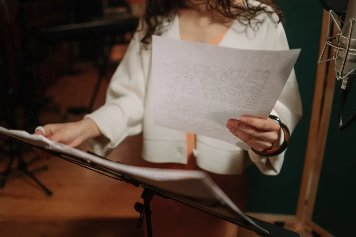 A female musician holds and reads lyrics on paper in a professional recording studio.